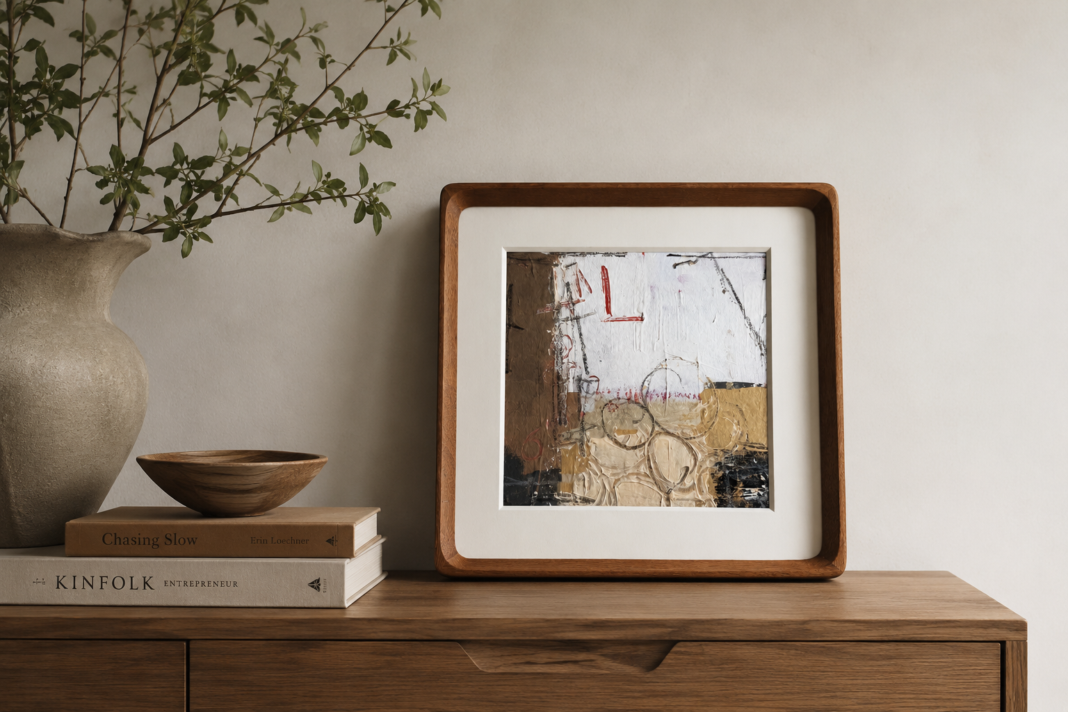 Framed artwork on a wooden surface with books and a vase in the background